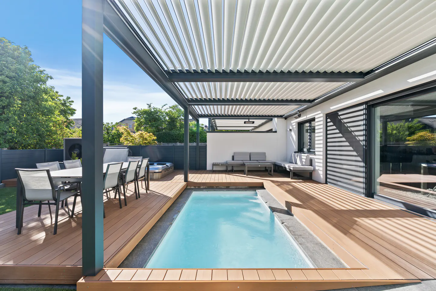 Outdoor patio with a small pool, dining table, and lounge area. The patio has a modern pergola and wood decking.
