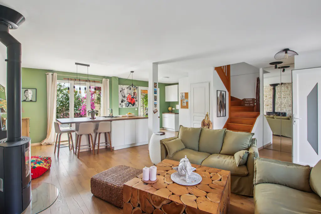 Open-plan living room with olive green sofa, unique wood-slice coffee table, wood stove, and kitchen with island seating.