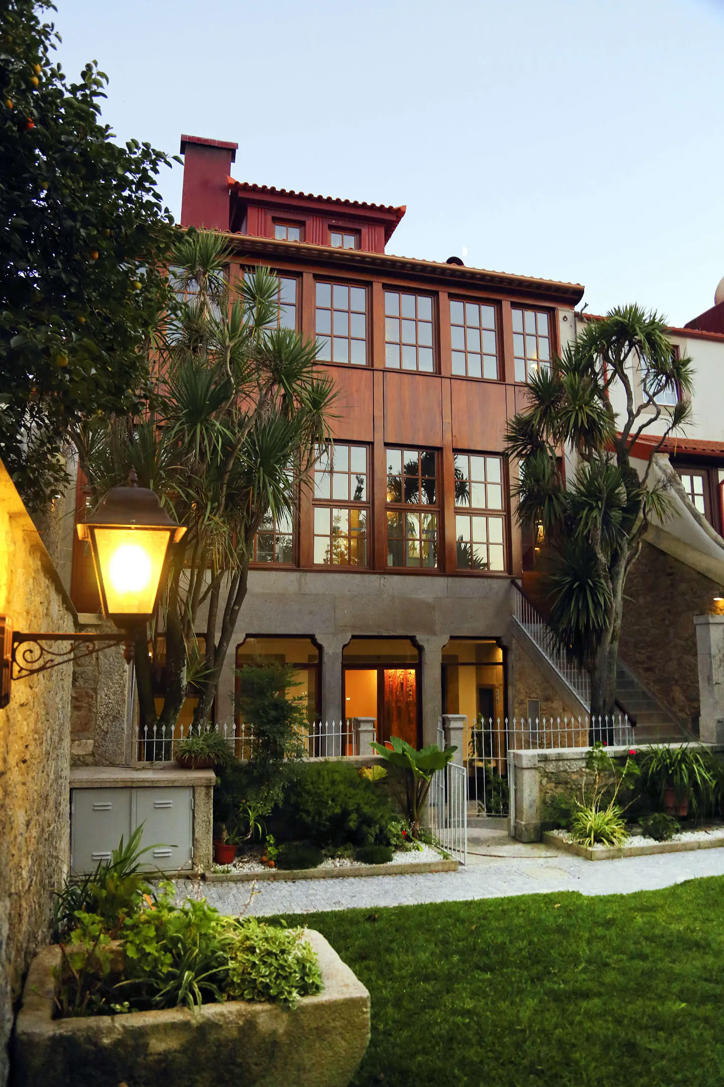 Exterior view of a three-story brown building with many windows, a stone base, and a green lawn in front.