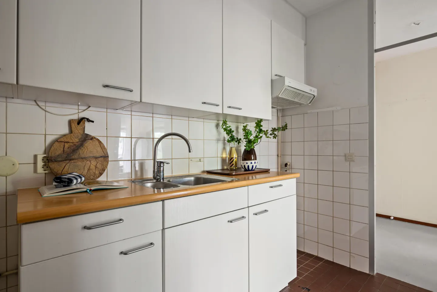 Kitchen with white cabinets, wood countertop, stainless steel sink, tiled backsplash, and a doorway to another room.