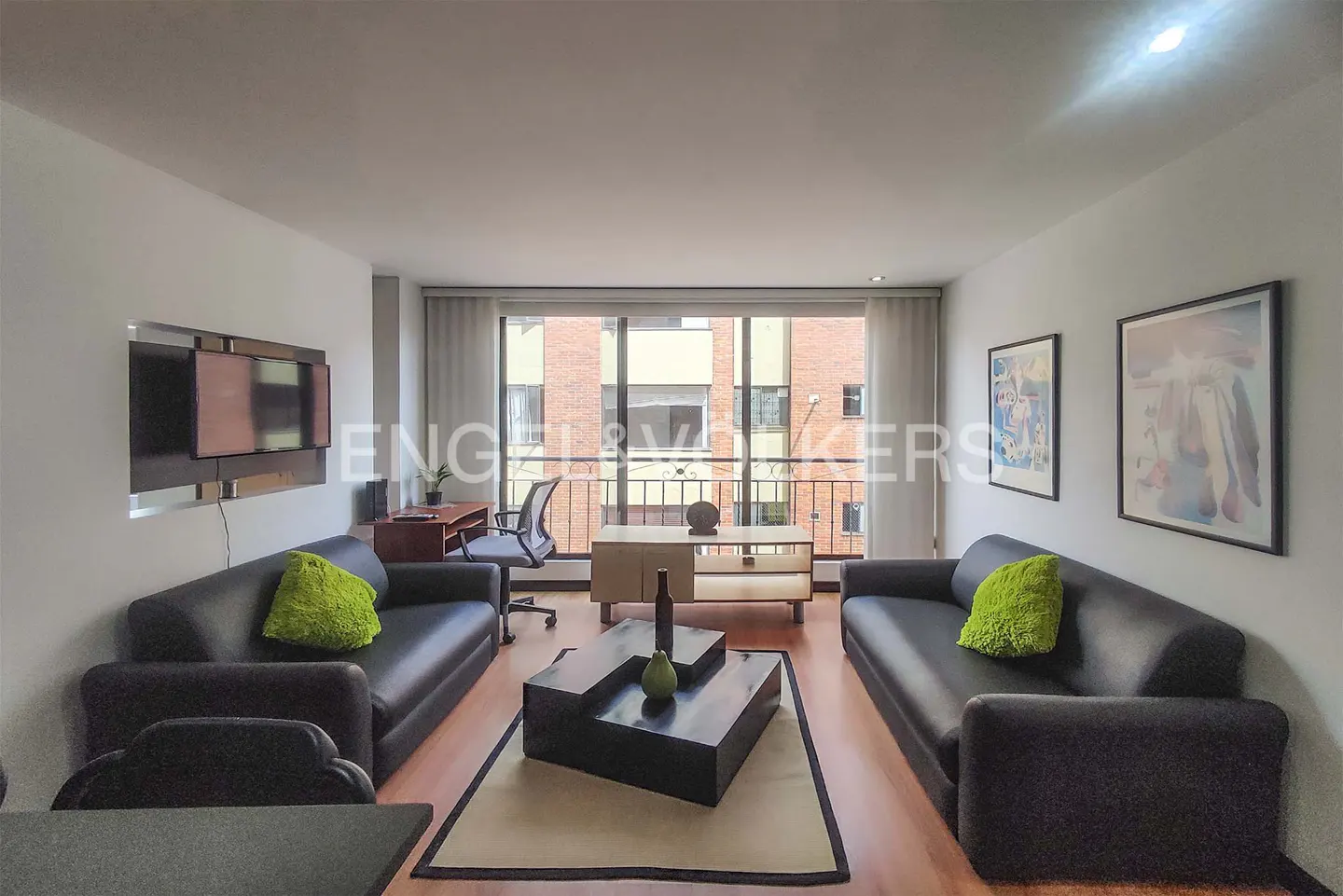 Living room with two black sofas, green pillows, a black coffee table, and a desk with a chair near a window.