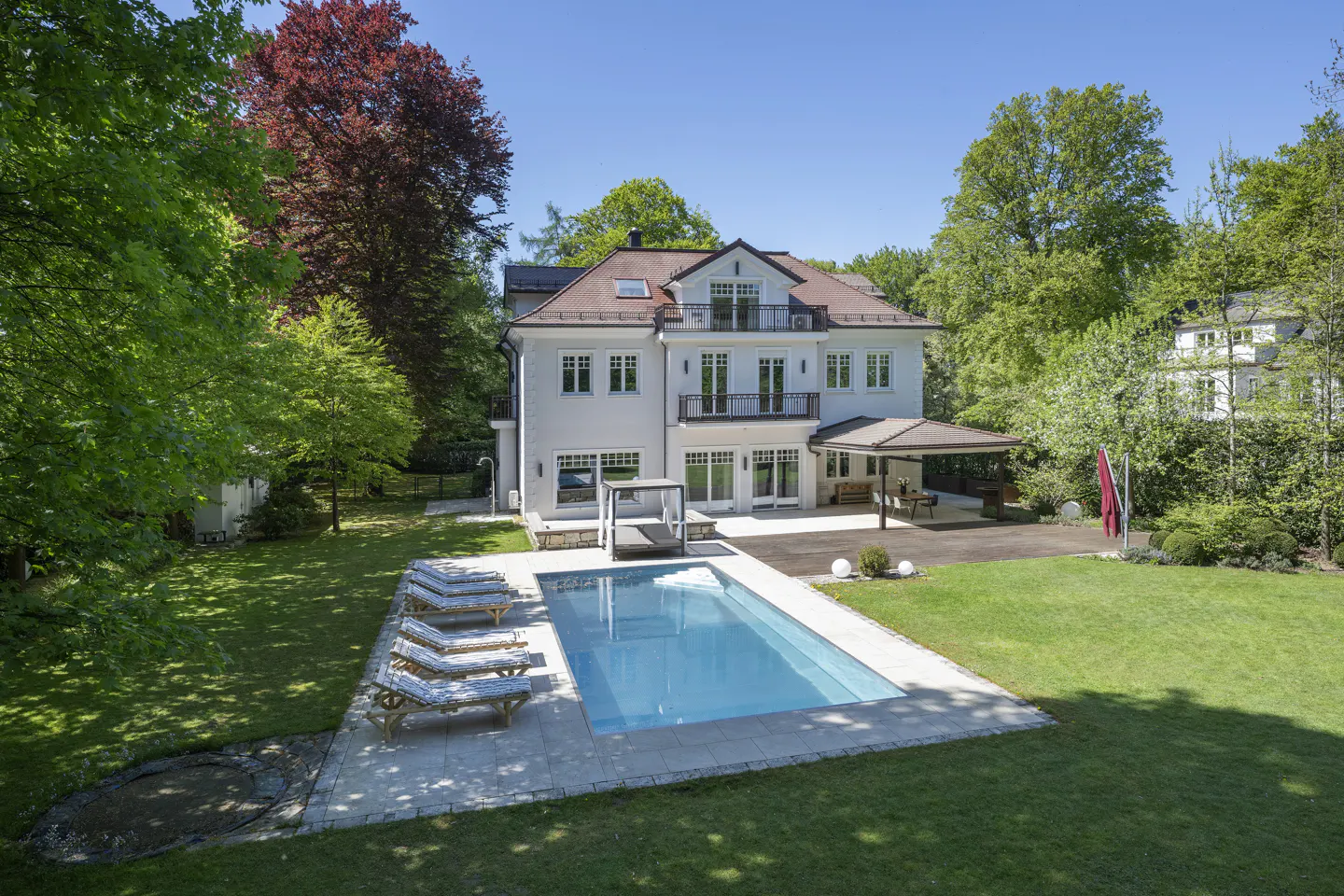 Aerial view of a white, two-story house with a pool, surrounded by green trees and lawn.