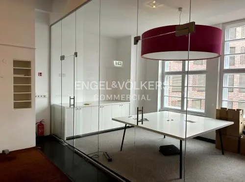 Office space with glass walls, a white conference table, and a large, round, maroon light fixture. Engel & Völkers logo visible.