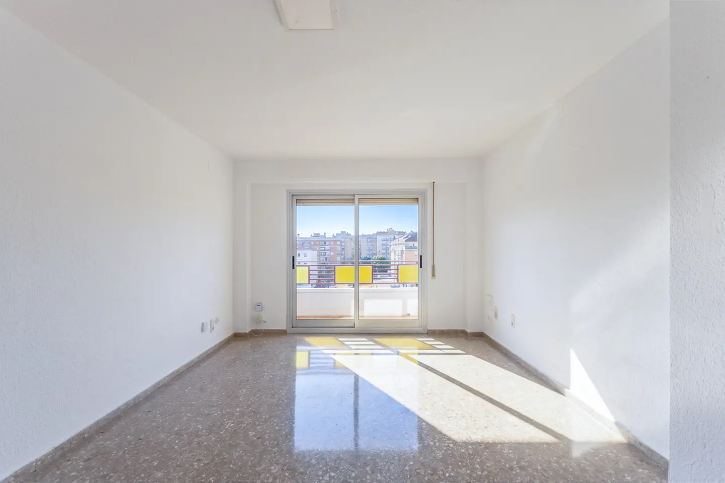 Empty room with white walls, speckled tile flooring, and a sliding glass door leading to a balcony with city views.