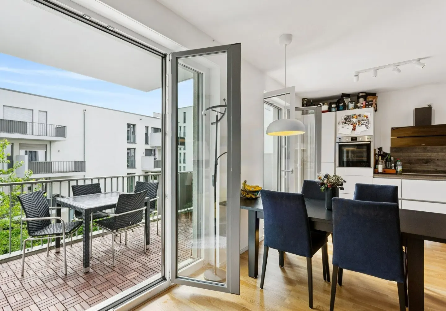 Modern dining room with dark blue chairs and a balcony featuring a table and chairs, overlooking a white apartment building.
