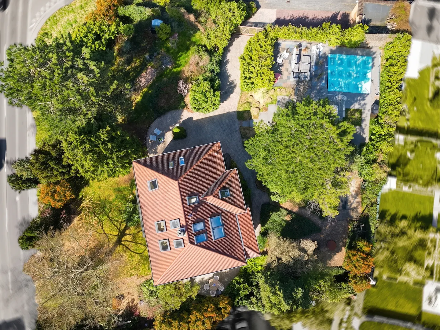 Aerial view of a house with a red tile roof, surrounded by green trees and a blue swimming pool.
