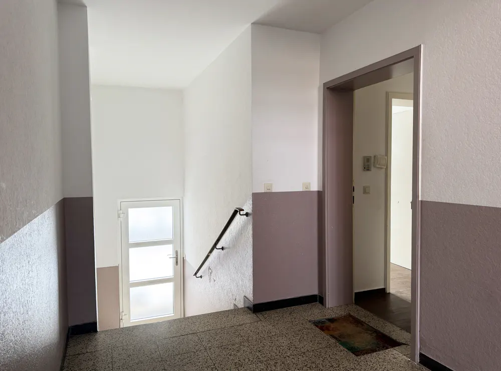 Interior view of a hallway with white and mauve walls, a doorway, and a staircase with a white door.