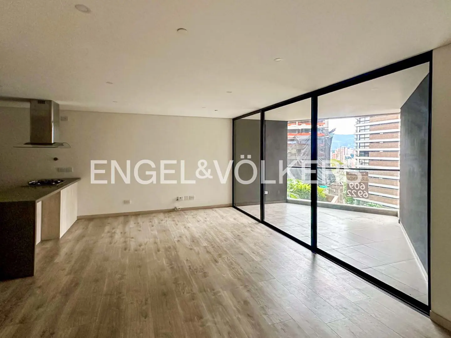Unfurnished apartment with wood floors, white walls, and black-framed sliding glass doors to a balcony with a city view.