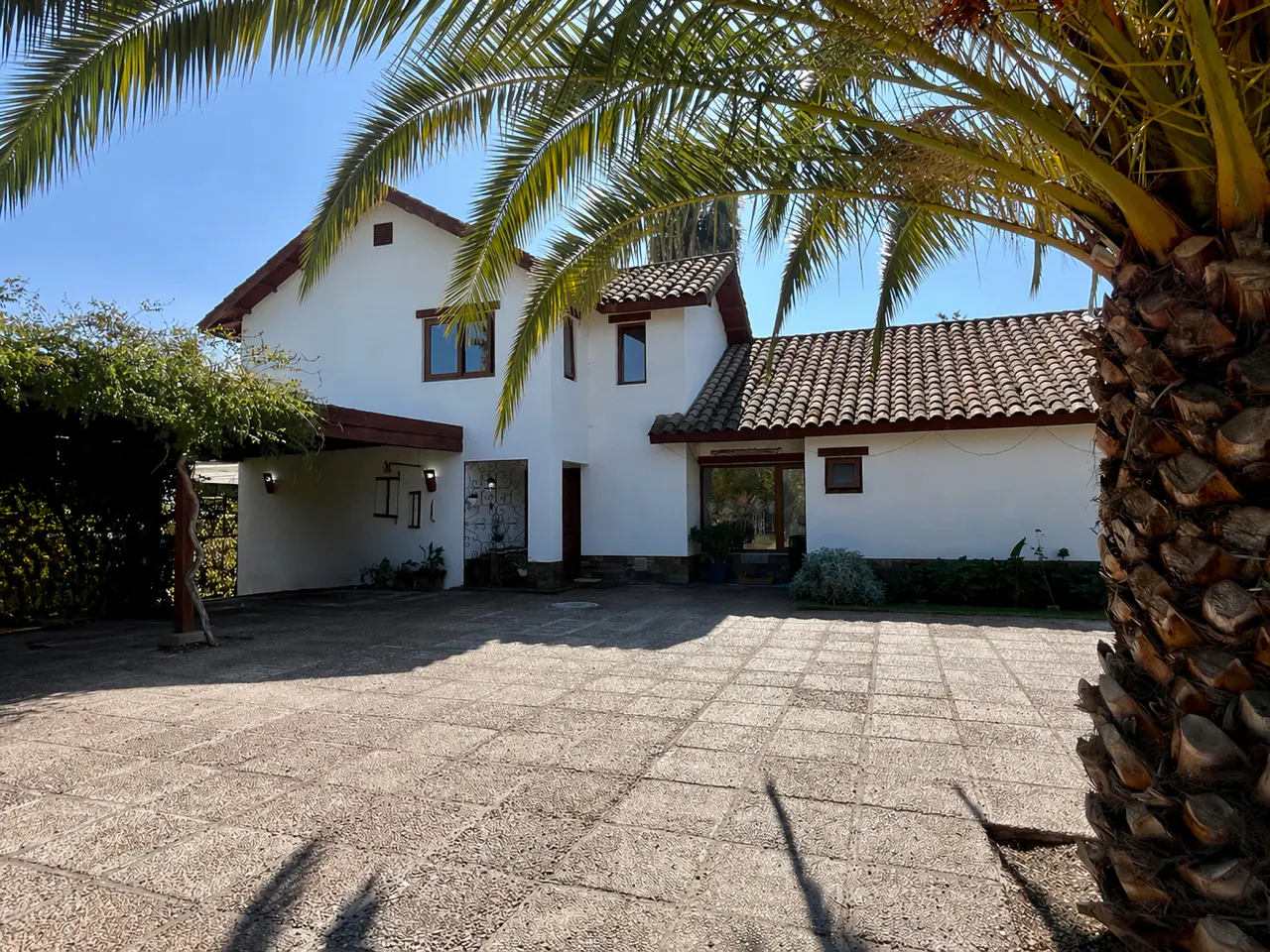 Exterior of a two-story white house with a brown tile roof and a stone driveway, framed by a palm tree.