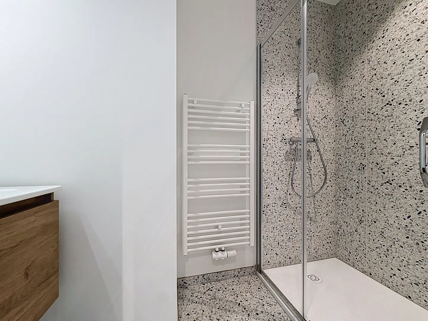 Modern bathroom with terrazzo walls, glass shower, white towel warmer, and wood vanity.