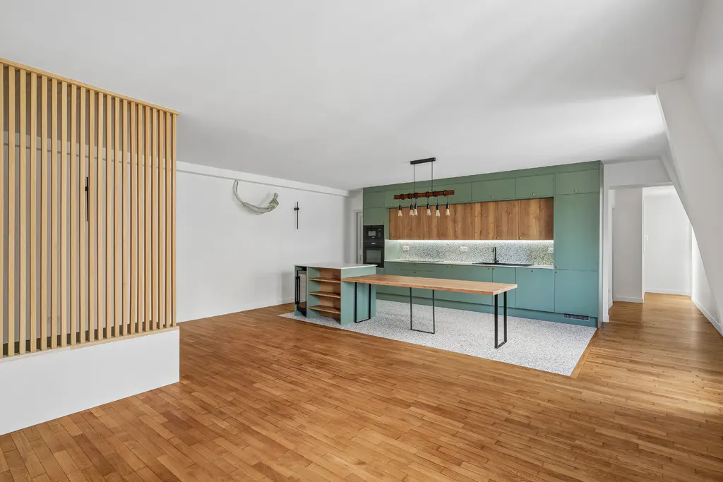 Open-concept kitchen with wood floors, green cabinets, and a wood slat partition. A long wood table sits in front of the island.