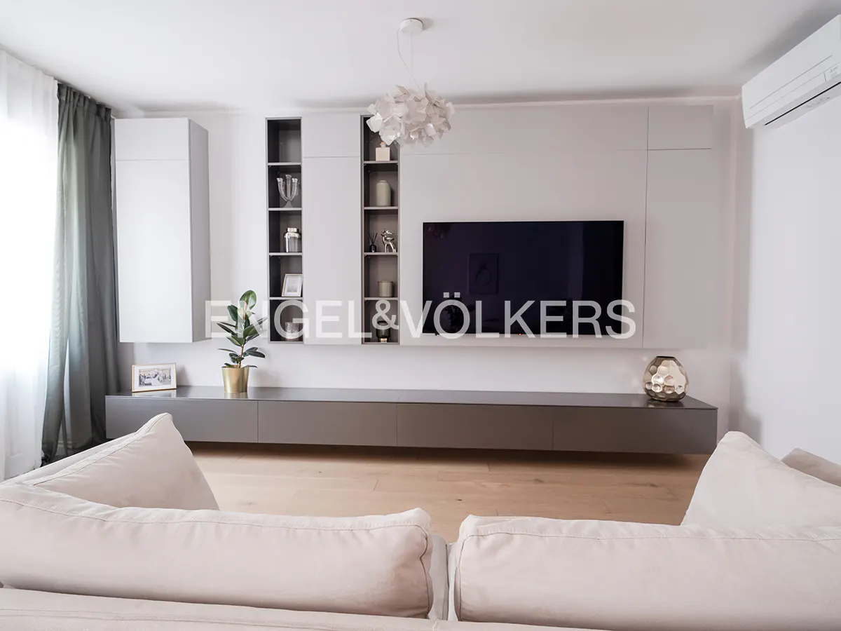 Living room with a large TV, white cabinets, and a gray console table. A beige sofa is in the foreground.