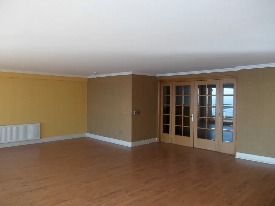 Empty room with wood floors, yellow and brown walls, and glass doors to a balcony with an ocean view.