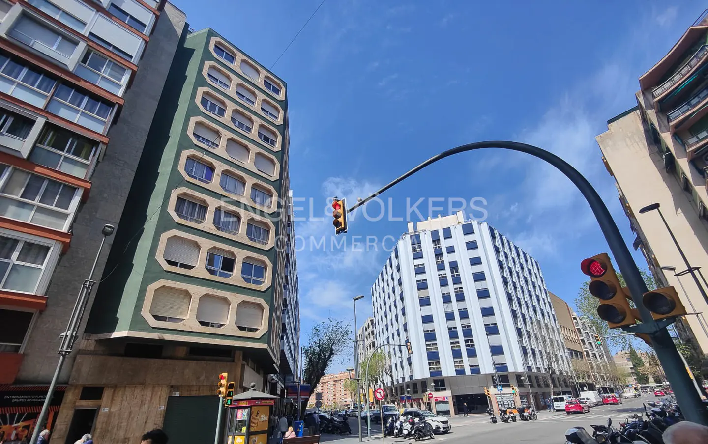 Street view of tall buildings, traffic lights, and vehicles on a sunny day.