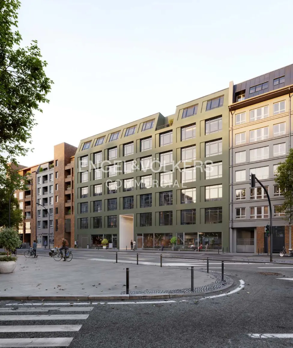 Exterior view of a modern, multi-story green building with many windows, and the Engel & Volkers logo. People and bikes are on the plaza.