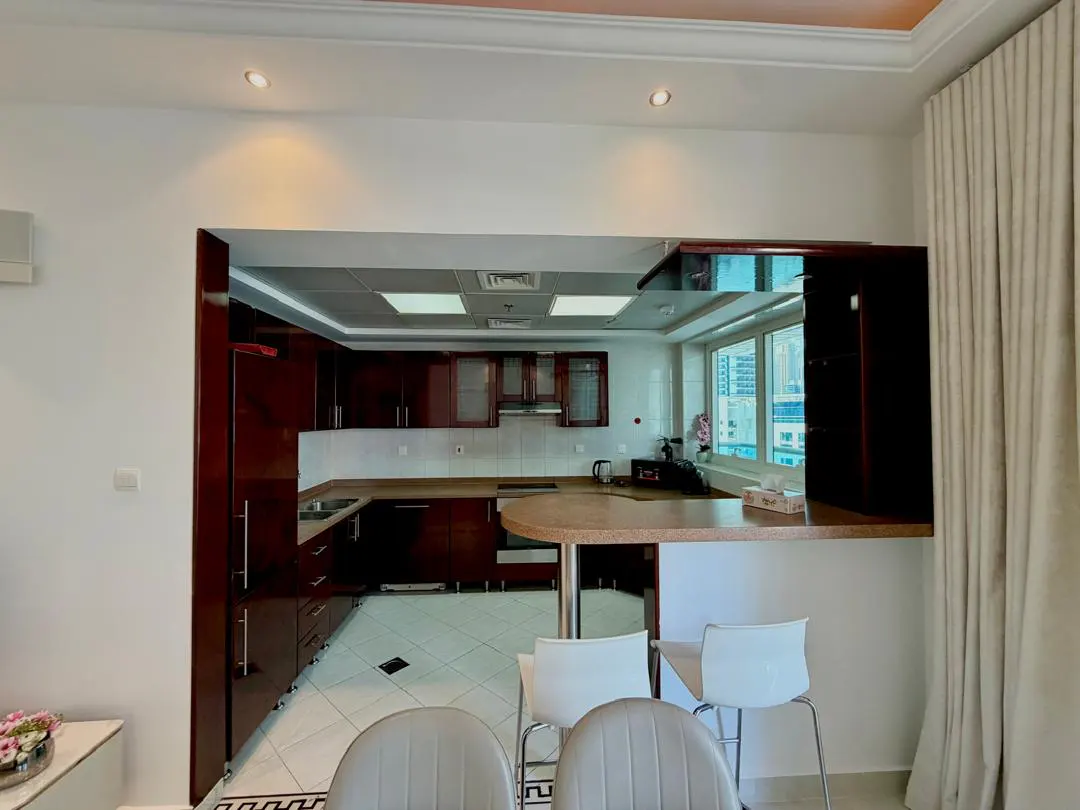 Modern kitchen with dark wood cabinets, white tiled floors, and a breakfast bar with two white stools.