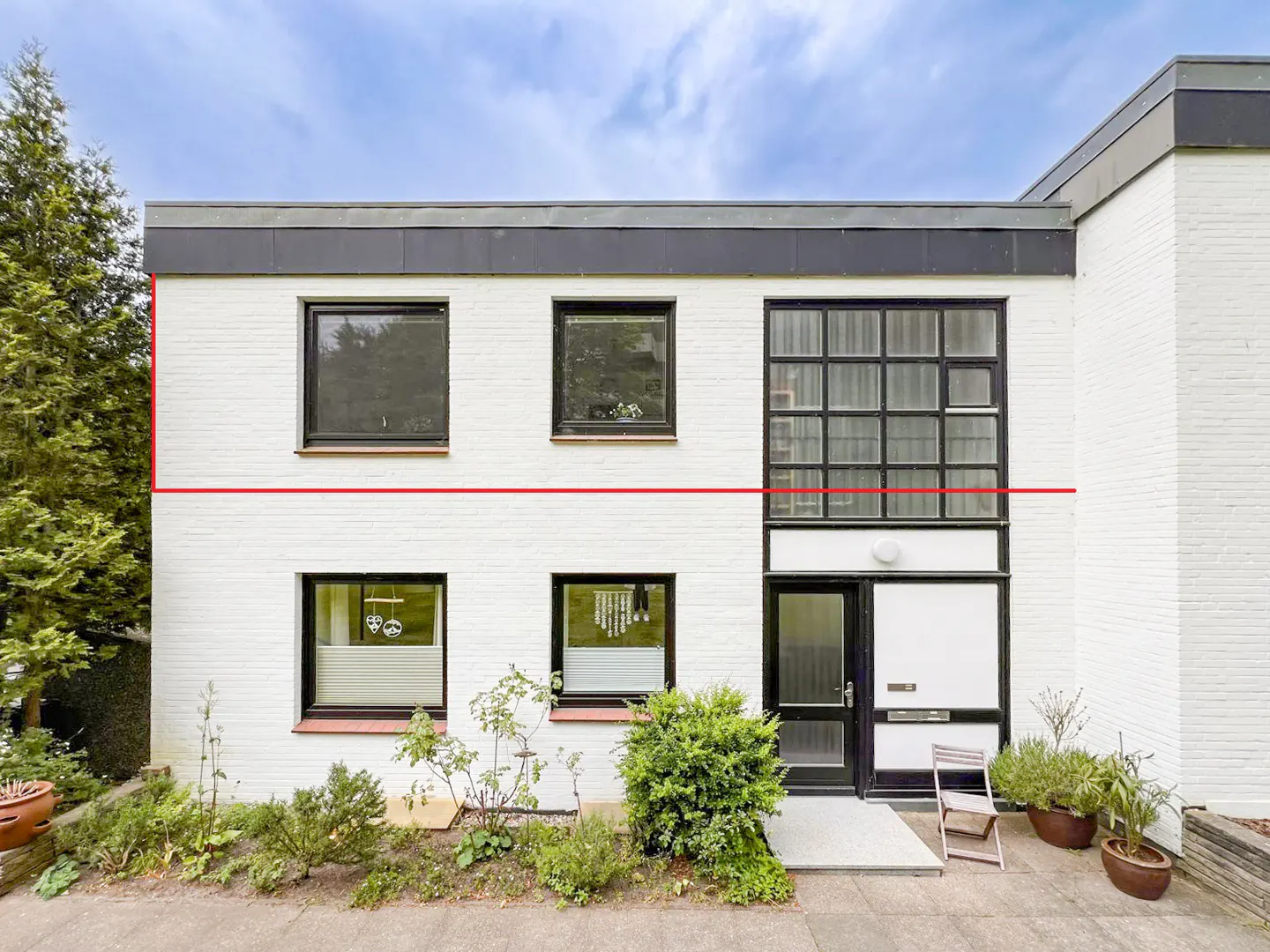 Two-story white brick house with black trim, windows, and flat roof. A small garden and walkway lead to the front door.