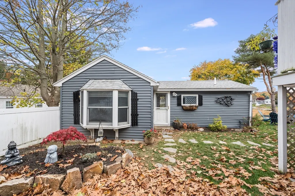 A gray, single-story home with a bay window, stone path, and autumn leaves scattered across the lawn.