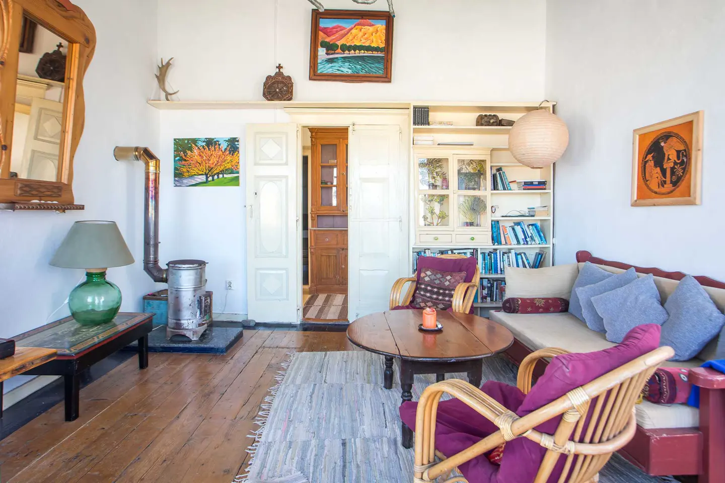 Cozy living room with a wood stove, round wooden coffee table, wicker chairs, sofa with blue pillows, and wall art.