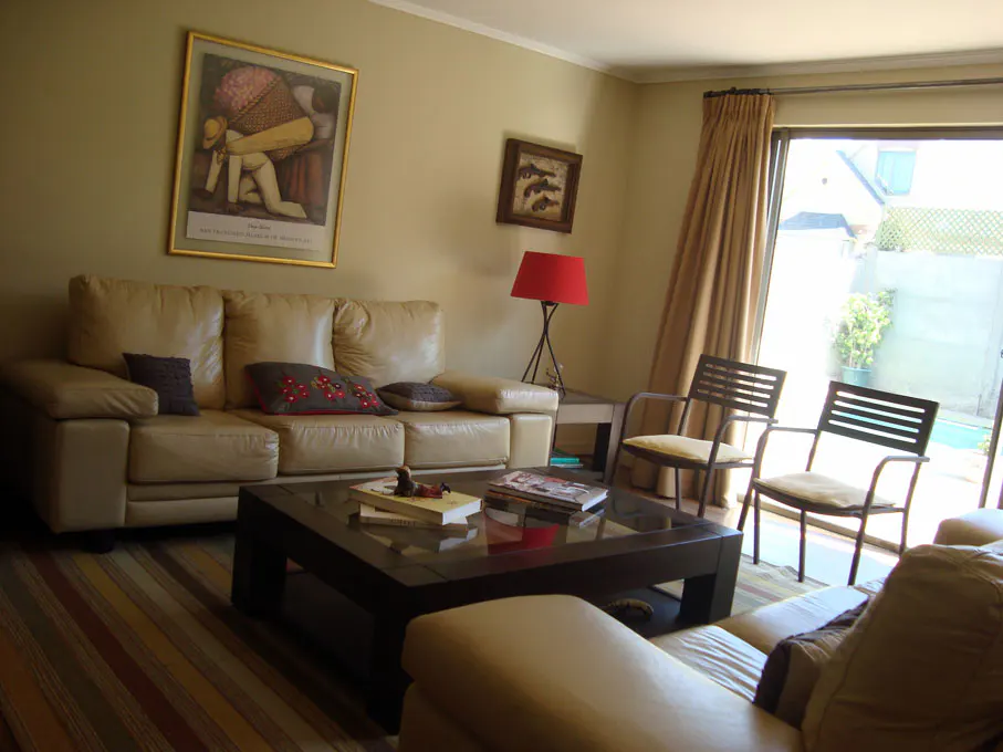 Living room with beige walls, a tan leather sofa, a dark wood coffee table, and two chairs near a sliding glass door.