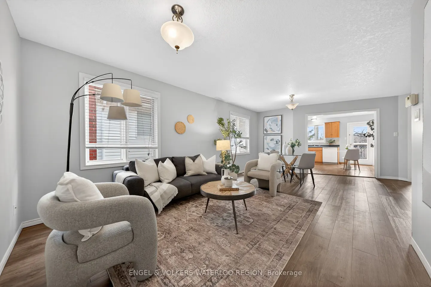 Living room with gray sofa, white pillows, patterned rug, and gray chairs. Kitchen visible in the background.