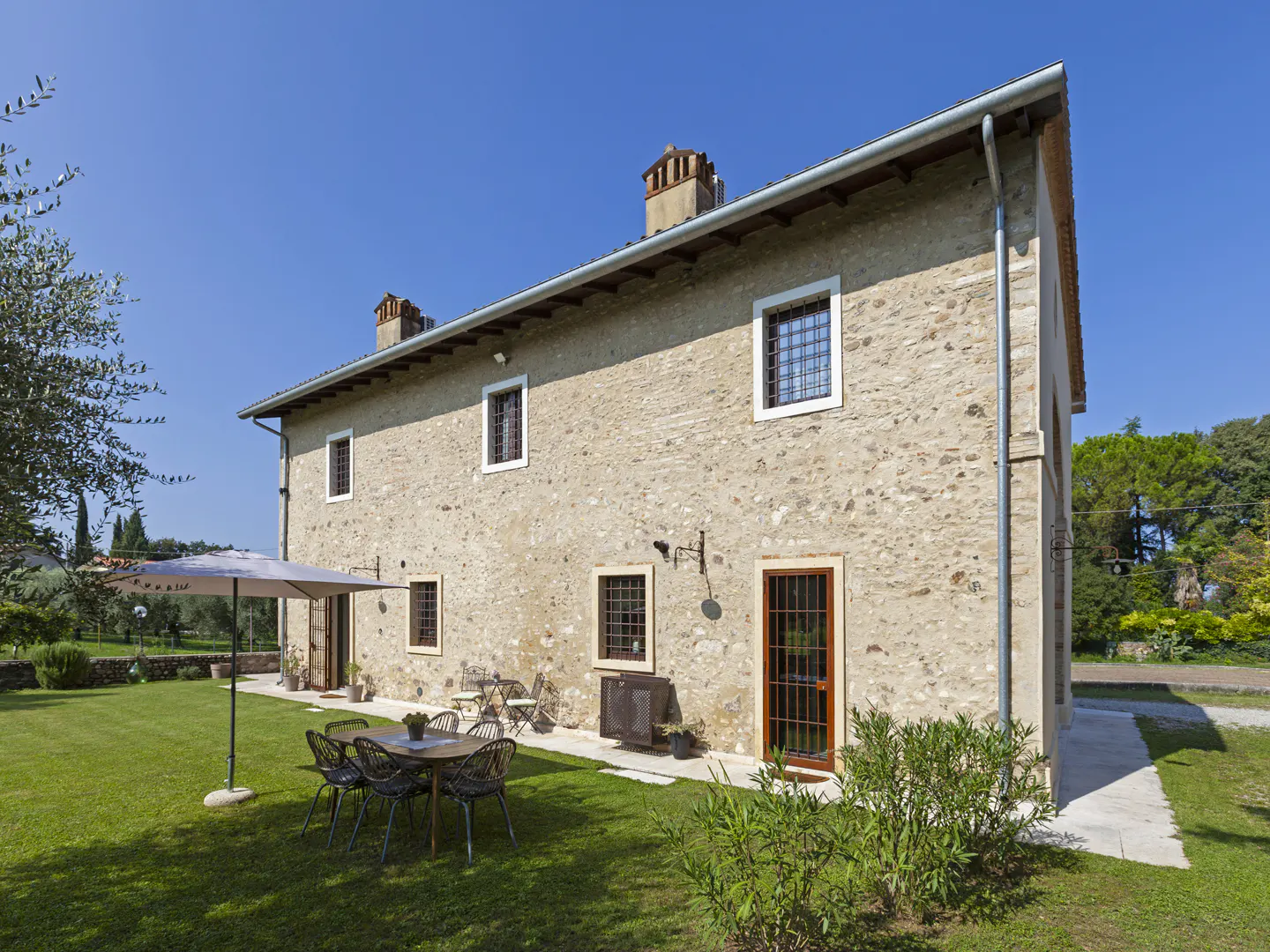 Exterior view of a two-story stone house with a green lawn, patio furniture, and a blue sky.