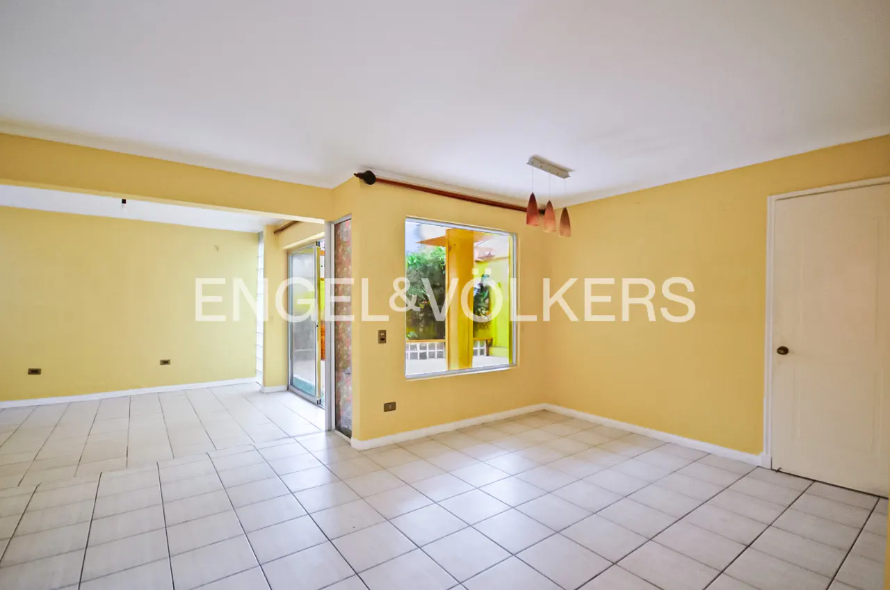 Empty room with yellow walls, white tile floor, and a window showing greenery outside. A white door is on the right.