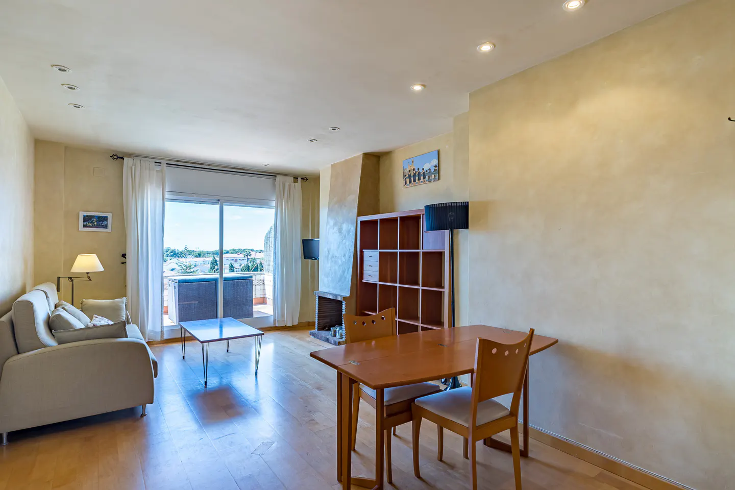Living room with beige sofa, wood floors, dining table, fireplace, and balcony with a view.