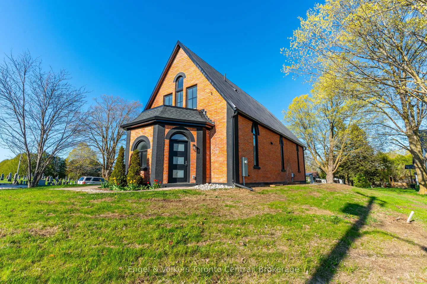 Exterior view of a brick building with a black roof and trim, set on a grassy hill under a blue sky.