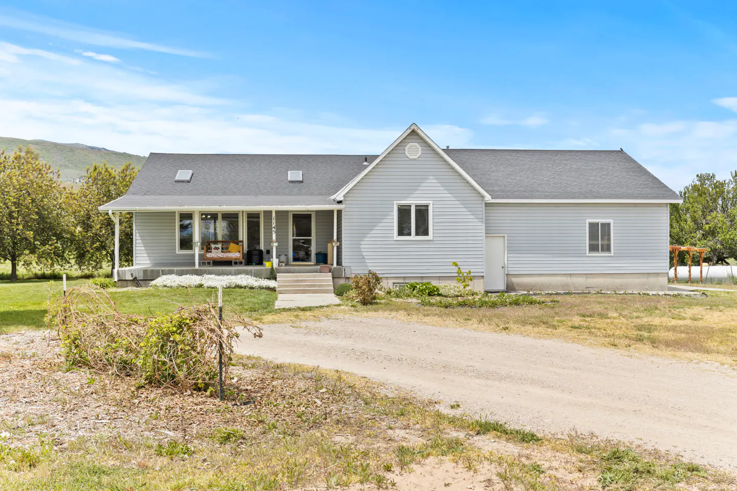 A light blue single-story house with a gray roof and a covered porch on a sunny day.