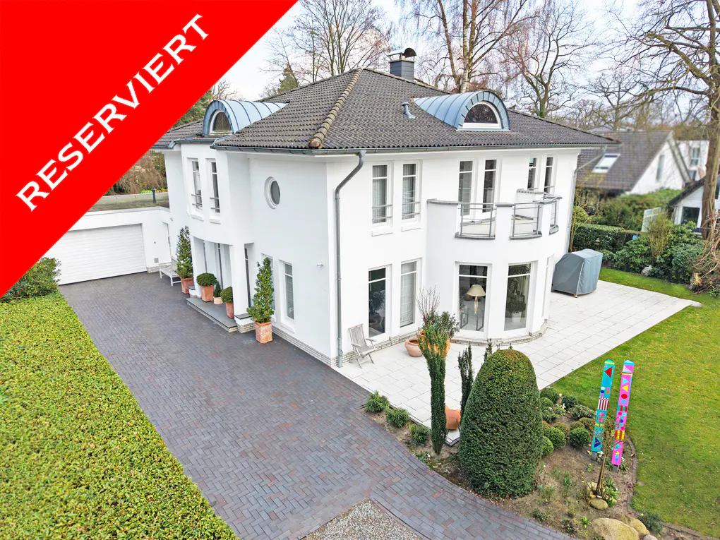 Two-story white house with a red "RESERVIERT" banner, a brick driveway, and green landscaping.