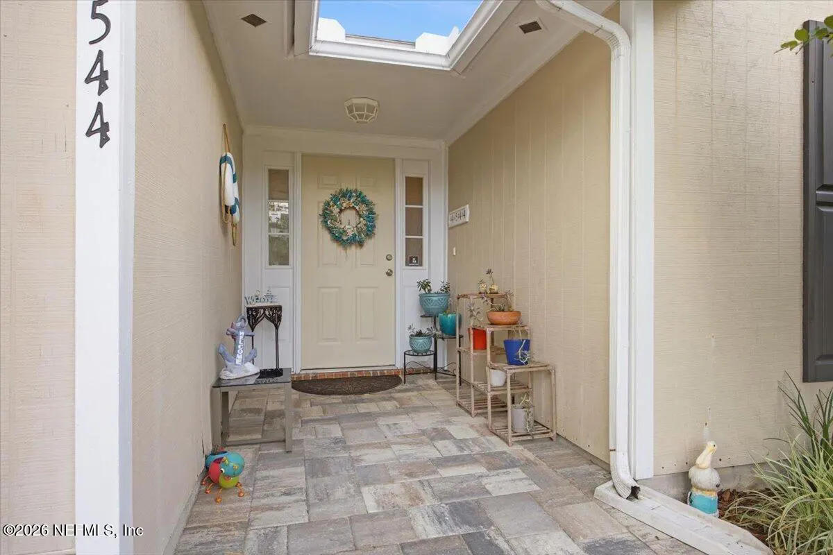 Covered porch with stone pavers leads to a cream-colored front door with a wreath. Potted plants and nautical decor add charm. House number 544 is visible.