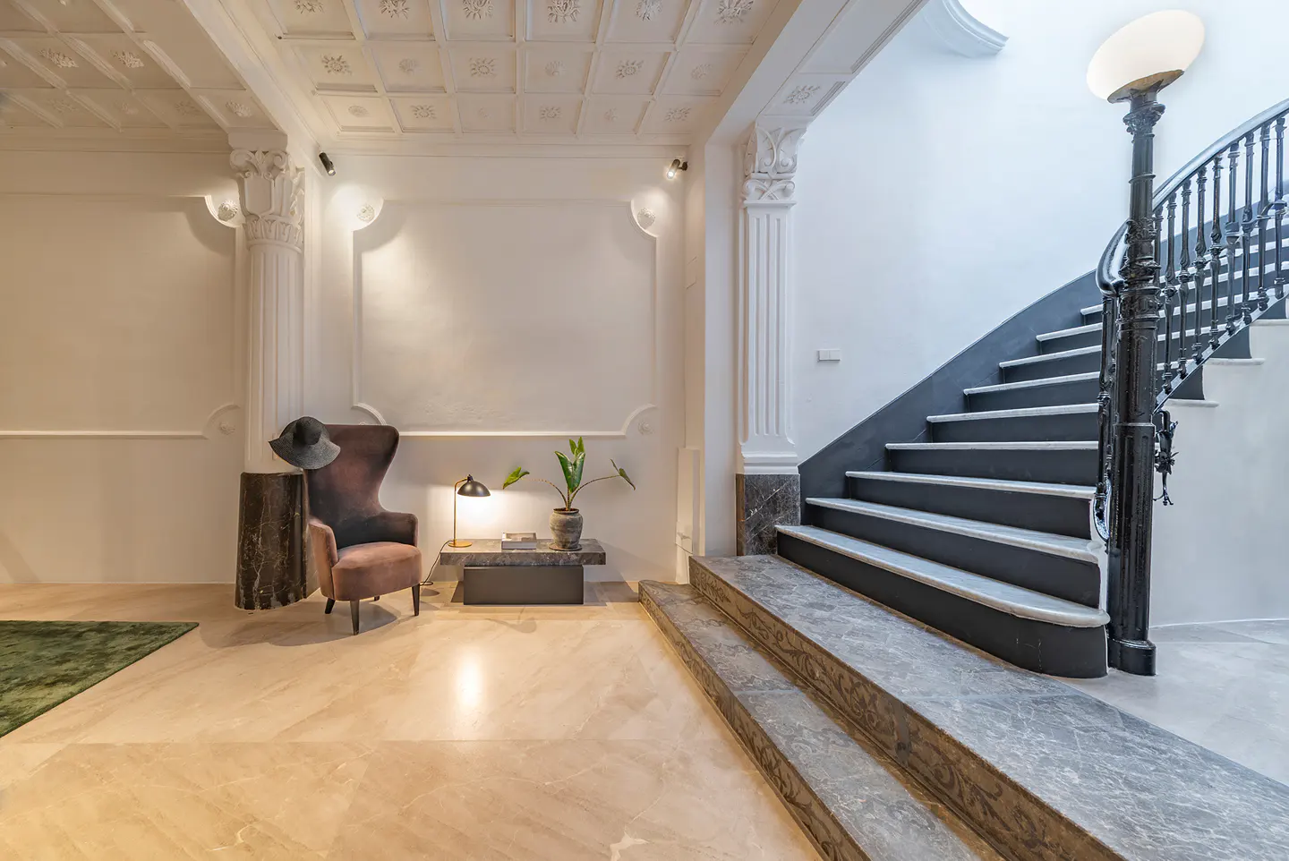 Elegant foyer with marble floors, a wingback chair, and a staircase with black railings and a vintage lamp post.