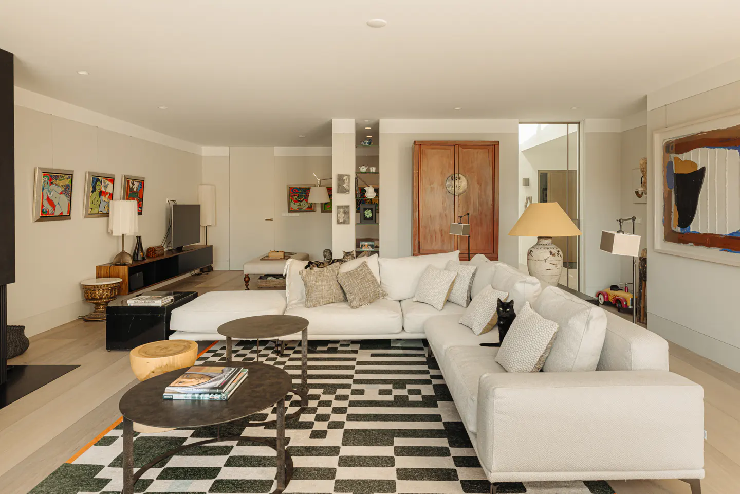 Bright living room with a white sectional sofa, black and white rug, and eclectic decor. A black cat sits on the sofa.