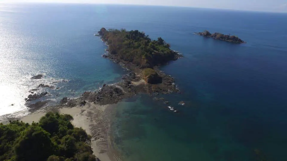 Aerial view of a tropical island with lush green vegetation, surrounded by turquoise and deep blue ocean waters.