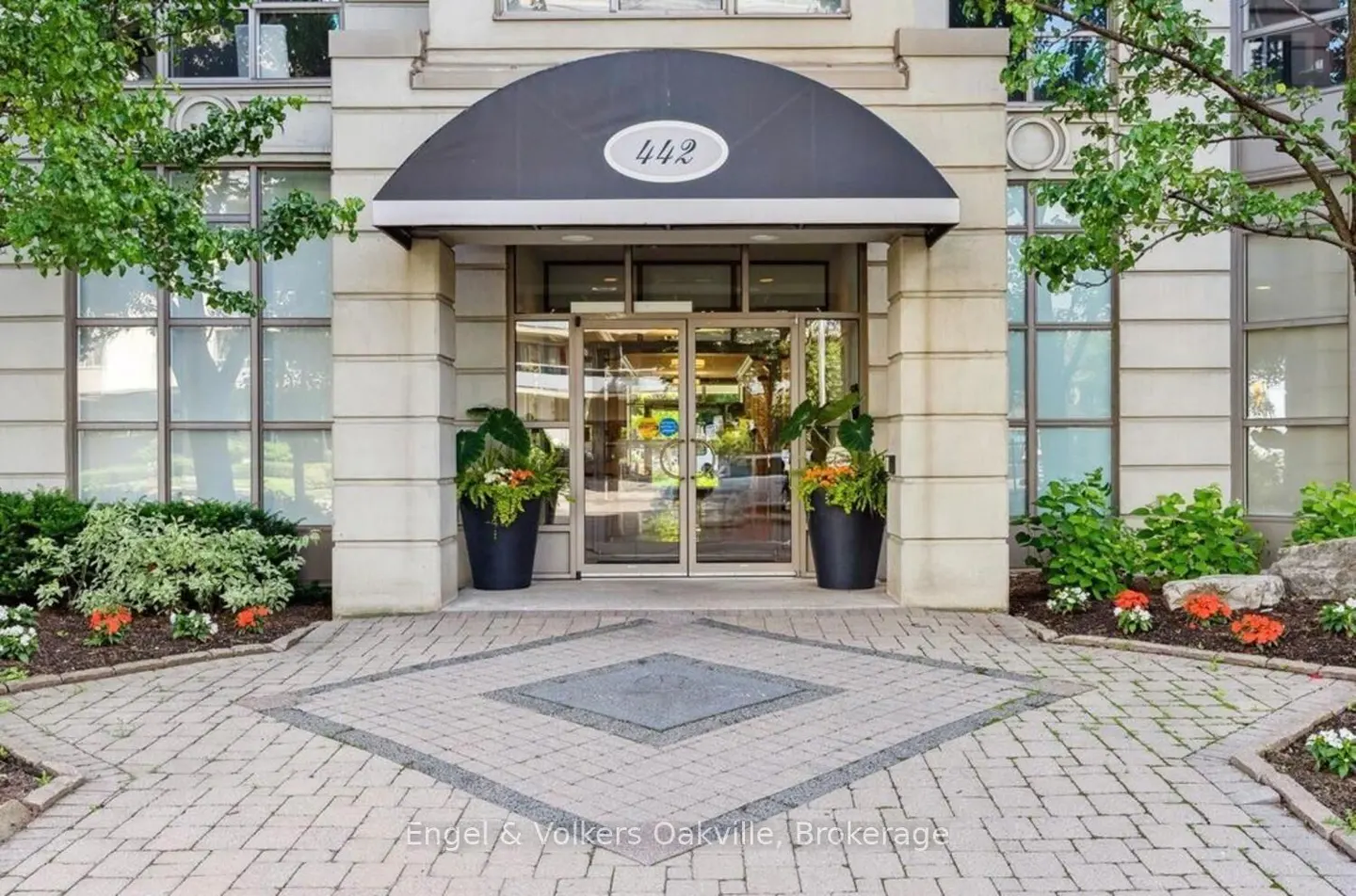 Building entrance with a black awning and "442" above glass doors. Potted plants flank the entrance on a brick walkway.