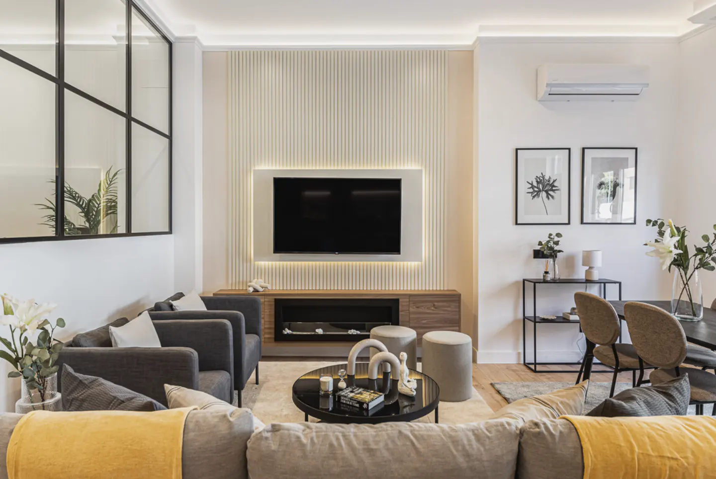 Living room with gray sofas, a black TV on a wood cabinet, and a black coffee table on a light rug. Two framed prints hang on the white wall.