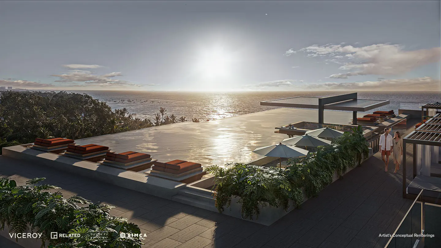 Rooftop infinity pool overlooking the ocean at sunset. Lounge chairs, umbrellas, and greenery surround the pool. A couple walks along the deck.