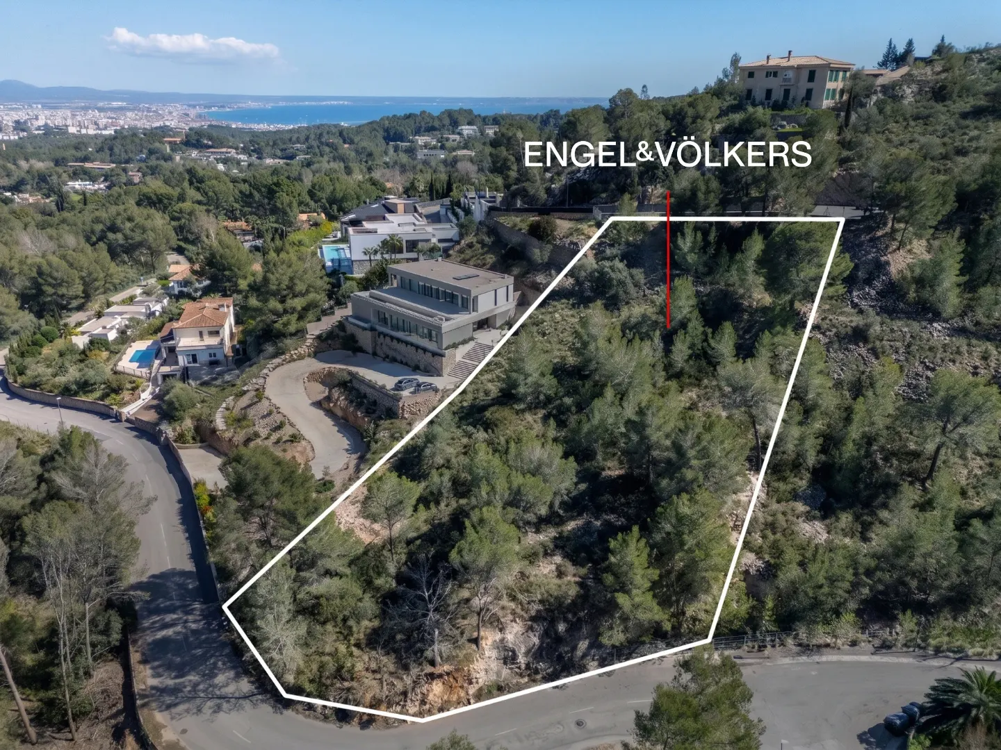 Aerial view of a wooded lot outlined in white, with a modern house nearby and Engel & Völkers logo.