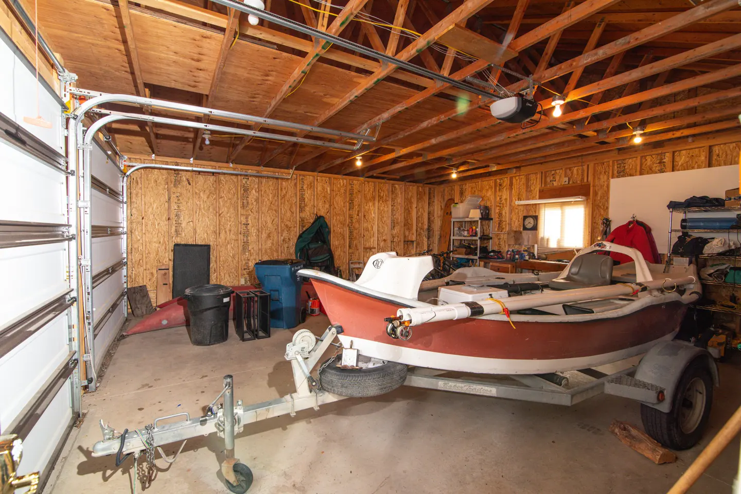 A garage with a red and white boat on a trailer, wood walls, and an open white garage door.