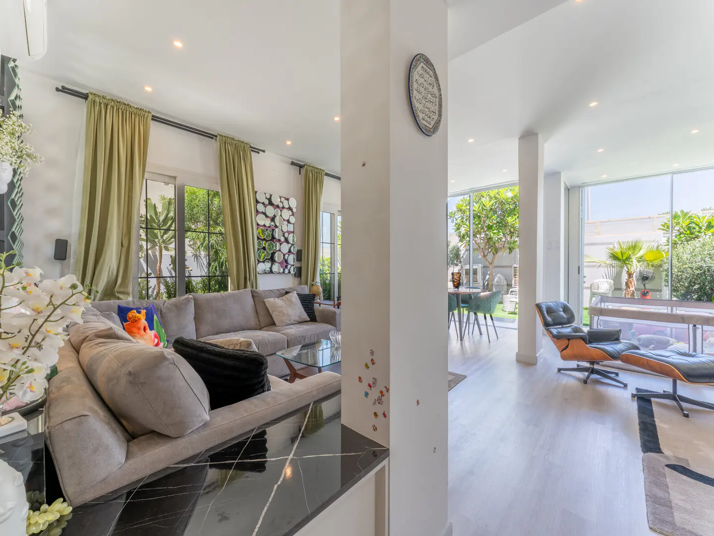 Bright, open-concept living space with gray sofas, black marble accents, and floor-to-ceiling windows overlooking a lush garden.