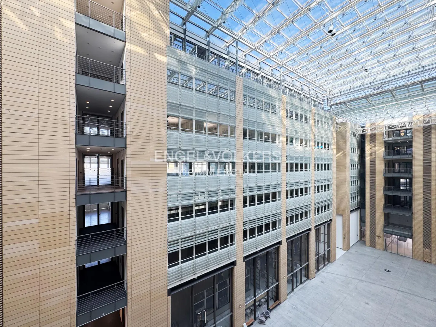 Interior view of a modern office building with a glass roof, beige walls, and multiple floors with windows.