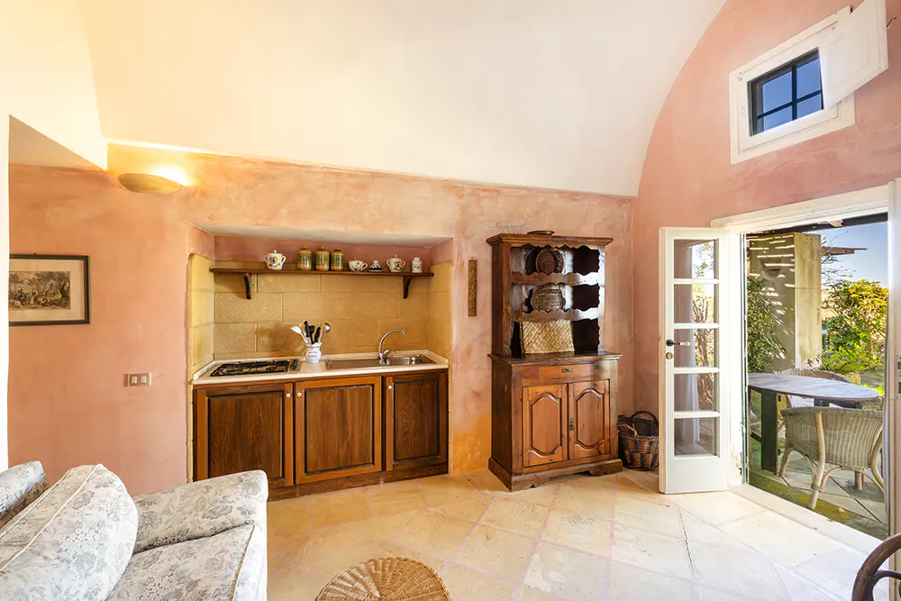 A cozy kitchen with pink walls, dark wood cabinets, and a stone floor. An open door leads to a patio with a table and chairs.