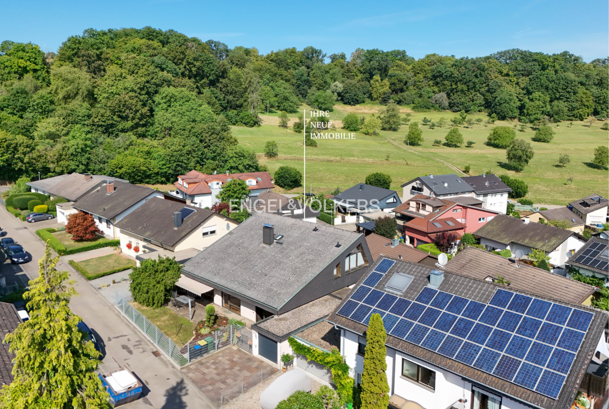 Aerial view of a residential neighborhood with houses, solar panels, and a large green field in the background.