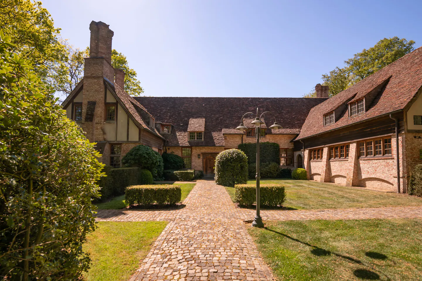 Exterior view of a large brick home with a brown roof, green bushes, and a stone walkway.