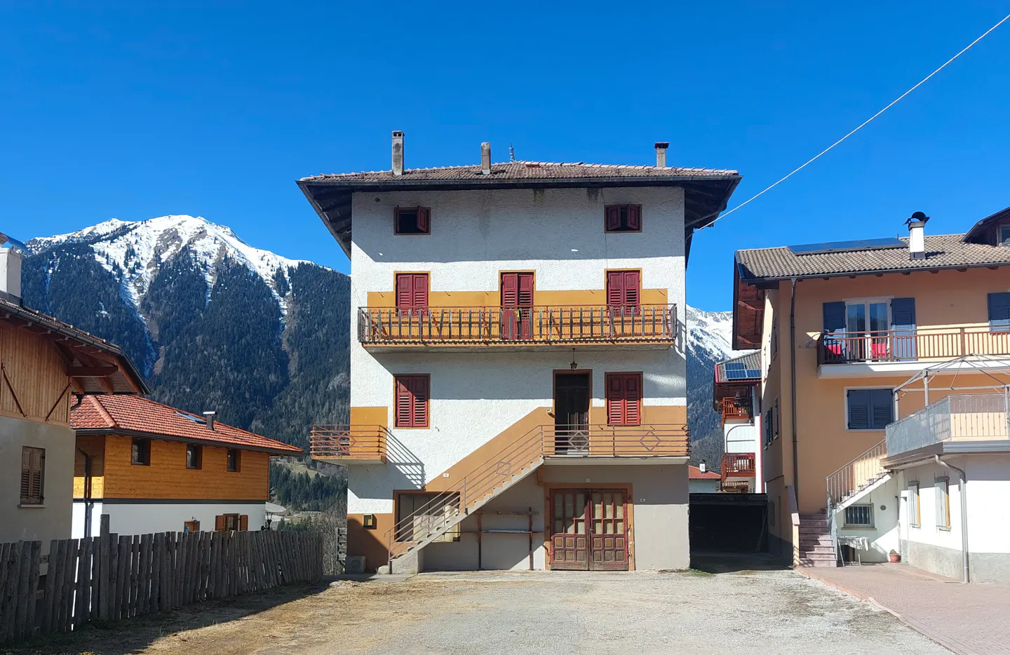 Three-story white building with red shutters and yellow trim, set against a mountain backdrop.
