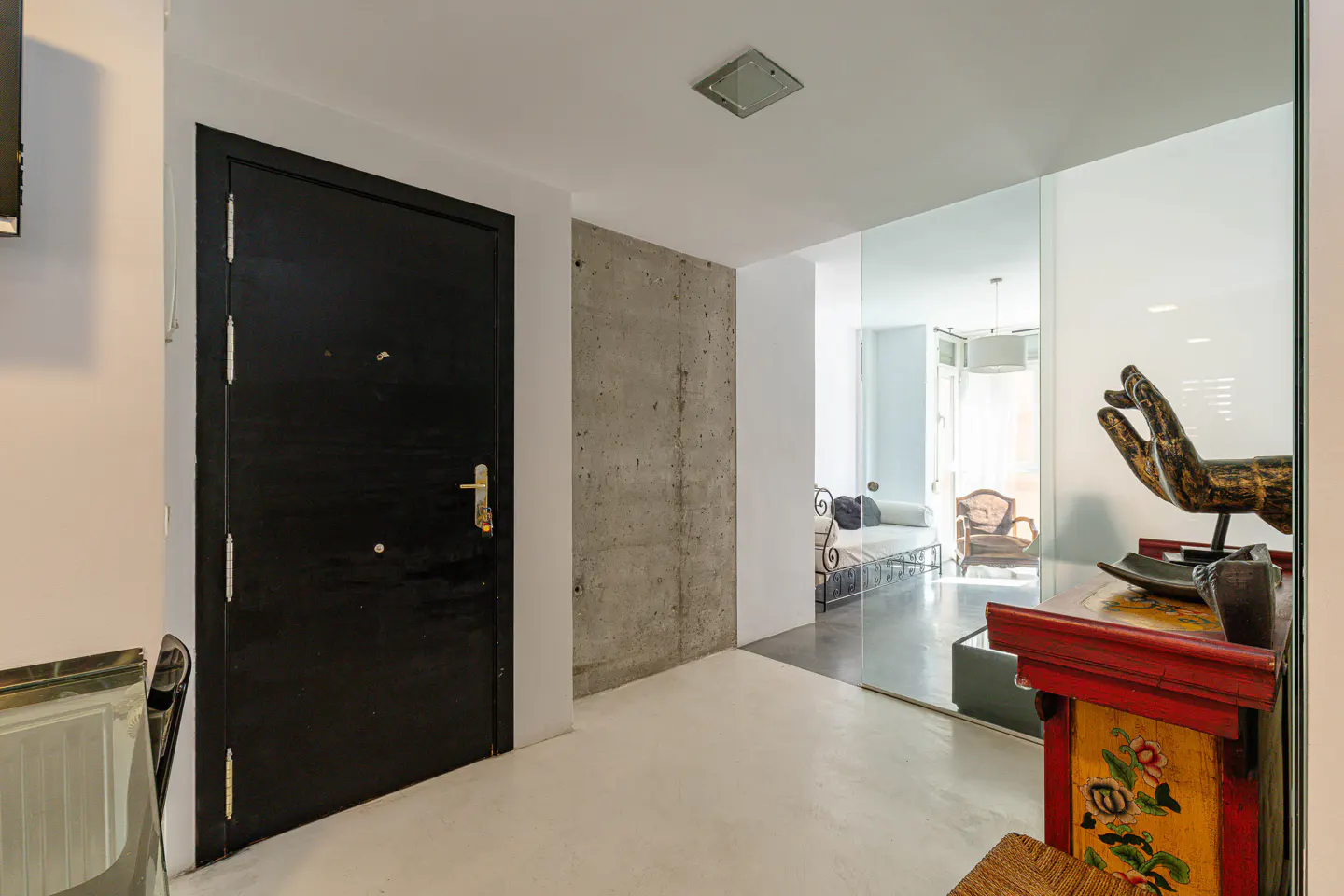 Modern entryway with a black door, concrete wall, and a decorative hand sculpture on a colorful painted wooden cabinet.