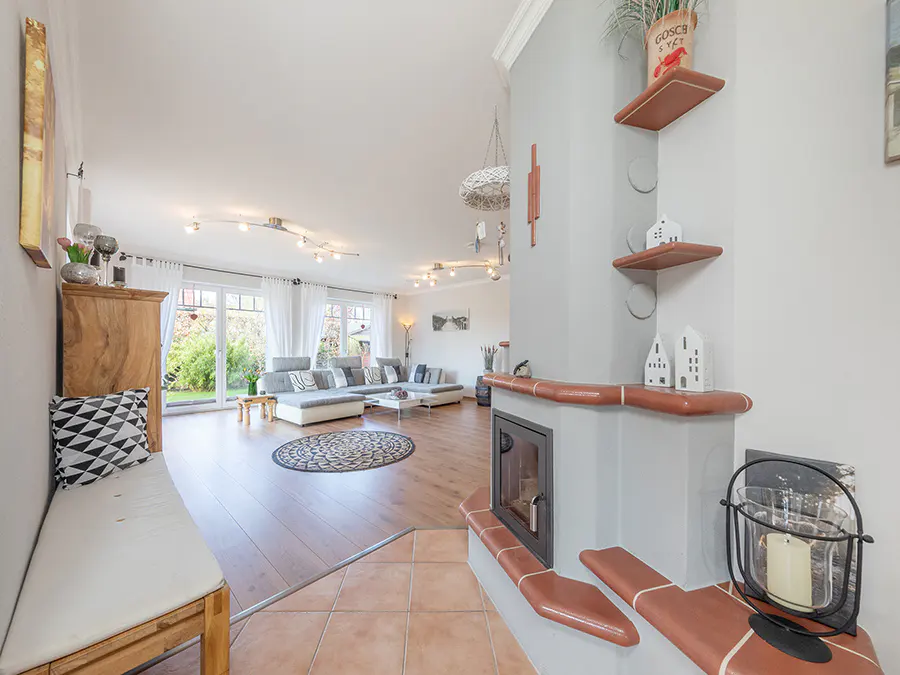 Bright living room with a gray fireplace, brown shelves, and a long gray sofa near large windows.
