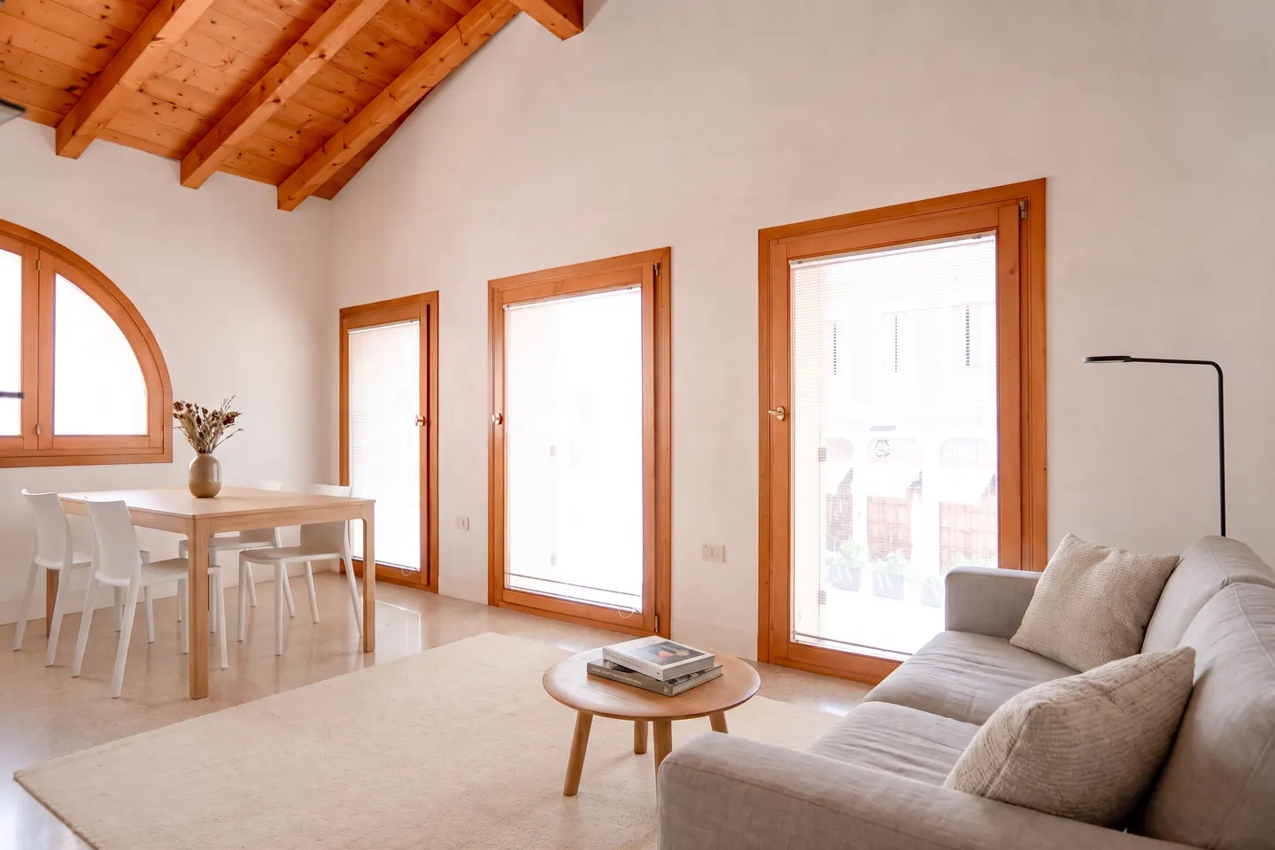 Bright living room with vaulted wood ceiling, white walls, dining area, and a beige sofa facing a small coffee table.