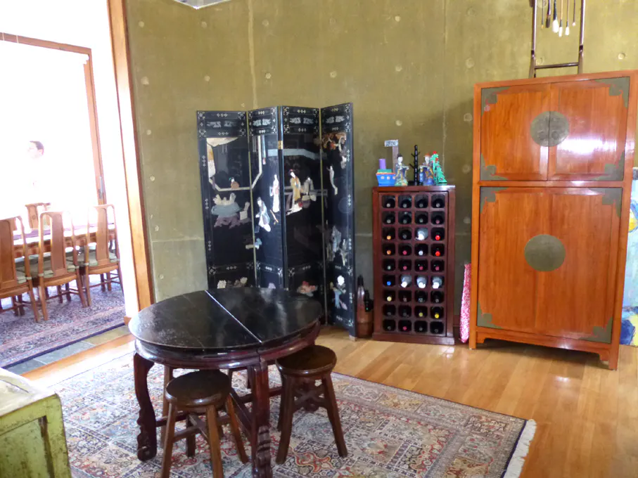 A room with a round table, stools, a black folding screen, a wine rack, and a wooden cabinet.
